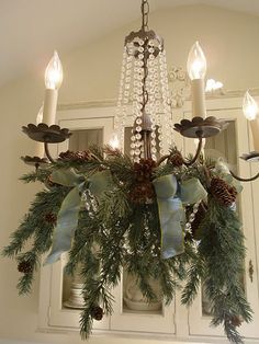 a chandelier hanging from the ceiling with pine cones and evergreen leaves on it