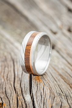 a wooden ring with silver and wood inlays on the outside, sitting on a piece of wood