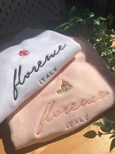 two towels with embroidered words on them sitting next to a potted plant in the background