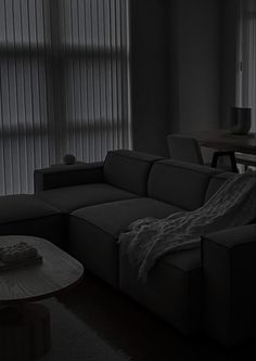 a living room with a couch, coffee table and blinds in the window behind it