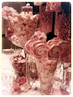 a table topped with lots of pink and white candies next to tall glass vases filled with candy