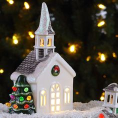 a small white church with a christmas tree in front of it and lights on the roof