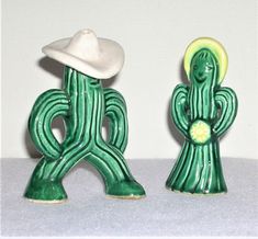 two green cactus figurines with a white hat on their head and one holding a flower