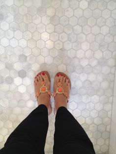 a woman's feet in sandals standing on a tile floor with hexagonal tiles