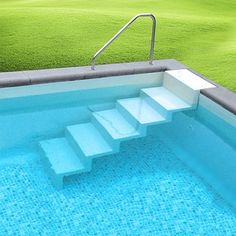 an empty swimming pool with steps leading up to the water and grass in the background