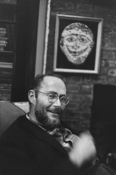 black and white photograph of man sitting in chair with brick wall behind him, smiling at camera