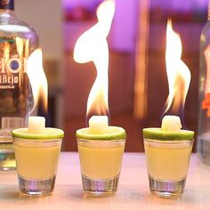 three shot glasses filled with drinks and lit candles