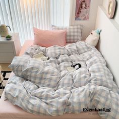 an unmade bed with plaid sheets and pillows in a small room next to a window