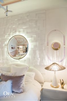 a white bed sitting under a round mirror in a room with two lamps on either side of it