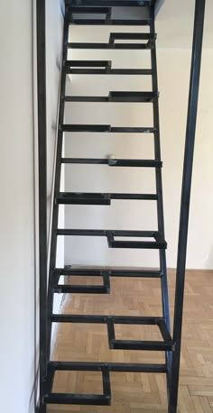 a set of black metal stairs in an empty room with hard wood flooring and white walls