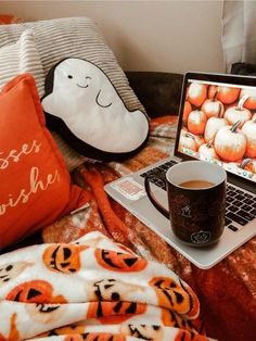 a laptop computer sitting on top of a bed next to a cup of coffee and a pillow