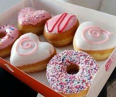 six donuts with pink frosting and sprinkles in a red box