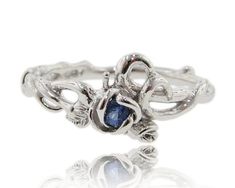 a silver ring with a blue stone in the middle and leaves around it, on a white background