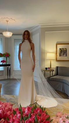 a woman in a white wedding dress standing next to a bouquet of flowers and a chandelier