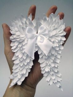 a hand holding two white paper flowers in it's palm, both with bows on them