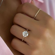 a woman's hand with a diamond ring on her finger and a pink flower in the background