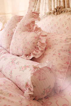 a bed with pink flowers and ruffled pillows on top of it's headboard