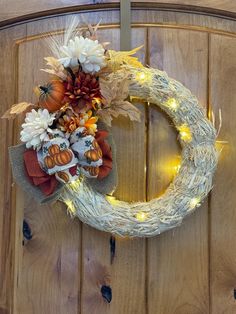 a wreath decorated with pumpkins and flowers on top of a wooden door frame at night