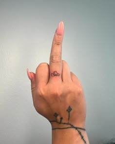 a woman's hand with a small tattoo on her left index finger pointing at the camera