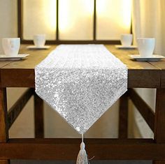 a white table runner with silver sequins and tassels on it, sitting on a wooden dining room table