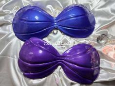 two purple plastic bowties laying on top of a white satin bed sheet with rings