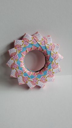 an origami flower with pink and blue flowers on it, sitting on a white surface