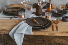 a table set with black plates and silverware, gold utensils and napkins