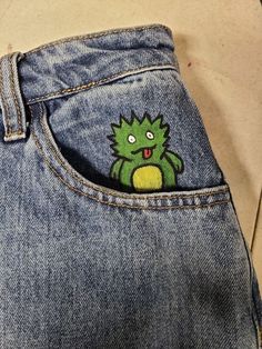 the back pocket of a pair of jeans with an embroidered green creature on it's side