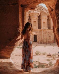 a woman standing in front of a rock formation looking out into the distance with her back to the camera