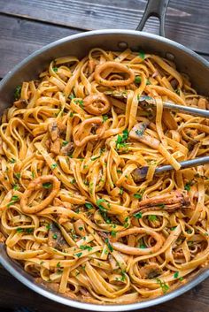 a skillet filled with pasta and parsley on top of a wooden table,