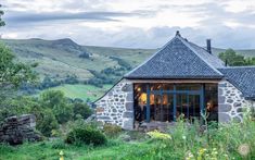 a stone building with a slate roof and windows in the middle of a grassy field