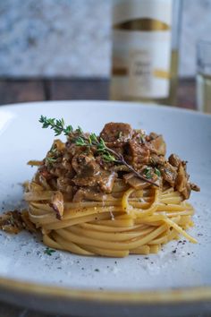 a white plate topped with pasta covered in meat and sauce next to a bottle of wine