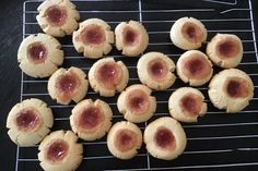 some cookies are cooling on a rack and have jam in the middle one cookie has been cut into small pieces