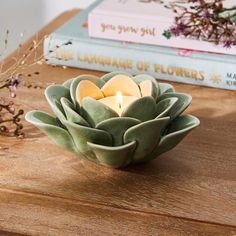 a candle that is on top of a table next to some books and flowers in the background