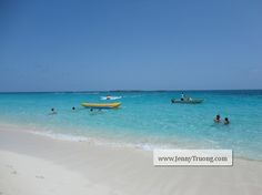 people are swimming in the clear blue water on a beach with boats and sand around them