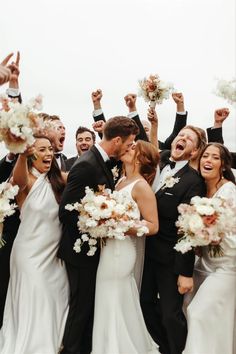 a group of people standing next to each other holding bouquets in the air with their hands up