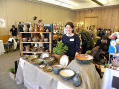 a woman standing in front of a table filled with pottery