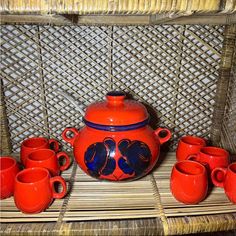 a red tea set with cups and saucers on a wicker tablecloth area