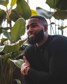 a man with a beard and black sweater standing in front of plants