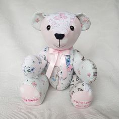 a pink and white teddy bear with flowers on it's chest sitting on a bed