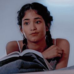 a woman laying on top of a bed next to an open book and looking at the camera