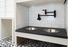 two stainless steel sinks in a black and white tiled bathroom with handrails on the wall