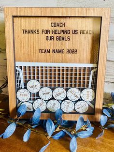 a wooden frame with some baseballs in it on a table next to blue leaves