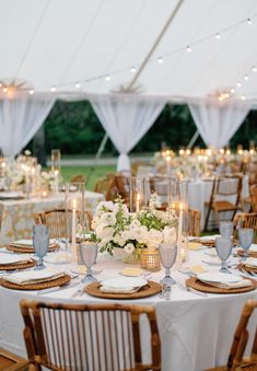 the tables are set up with white flowers and candles for an elegant wedding reception in a tent