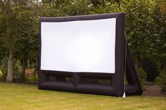 an inflatable movie screen sitting on top of a lush green field next to trees