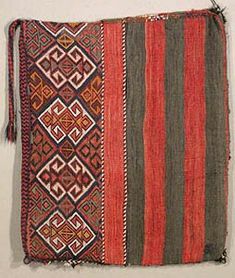 an old rug hanging on the wall in front of a white wall with a black and red stripe