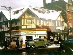 an old car parked in front of a building with people standing outside it on a snowy day