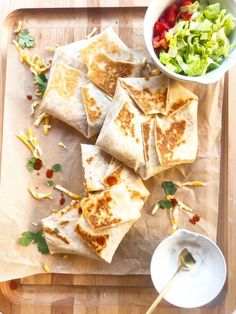 several quesadillas on a cutting board with a bowl of salad