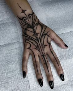 a woman's hand with black nail polish and tattoos on her left hand, which is decorated with an intricate design