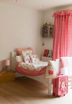 a bedroom with pink and white bedding, plaid curtains, and wooden flooring